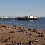 Plaja din Brighton cu oameni la soare și Palace Pier în fundal, imagine pentru concediu de odihnă în UK