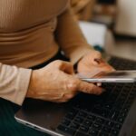 Settled status în 2026: o femeie își verifică statutul EUSS pe telefon, lângă laptop