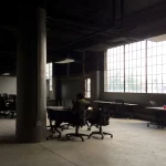Birou open-space luminat de ferestre mari, cu un angajat la laptop