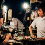 Angajat la tejgheaua unui restaurant care servește un client seara, imagine pentru ghidul despre hărțuirea la muncă de către clienți în UK