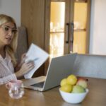 Femeie care analizează documente financiare la laptop, acasă
