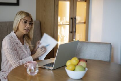 Femeie care analizează documente financiare la laptop, acasă