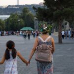 Mamă care ține de mână o fetiță cu ghiozdan pe drumul spre școală