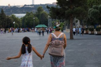 Mamă care ține de mână o fetiță cu ghiozdan pe drumul spre școală