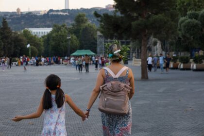 Mamă care ține de mână o fetiță cu ghiozdan pe drumul spre școală