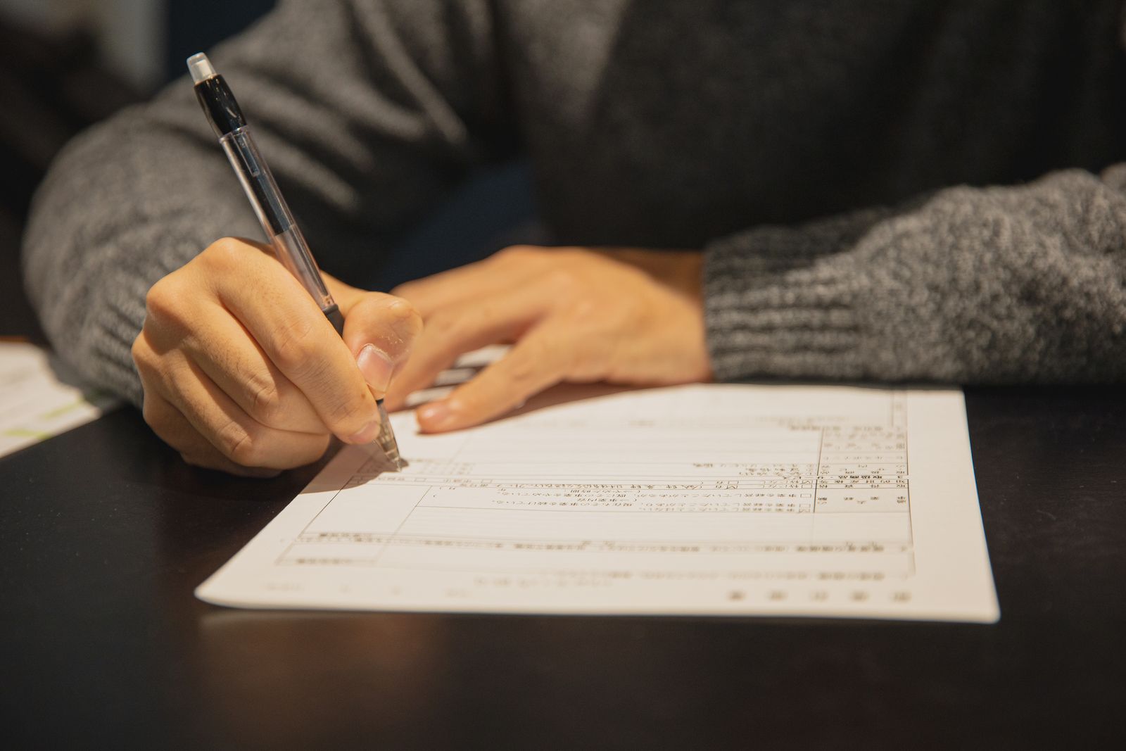 Mâini completând un formular, document oficial pe masă