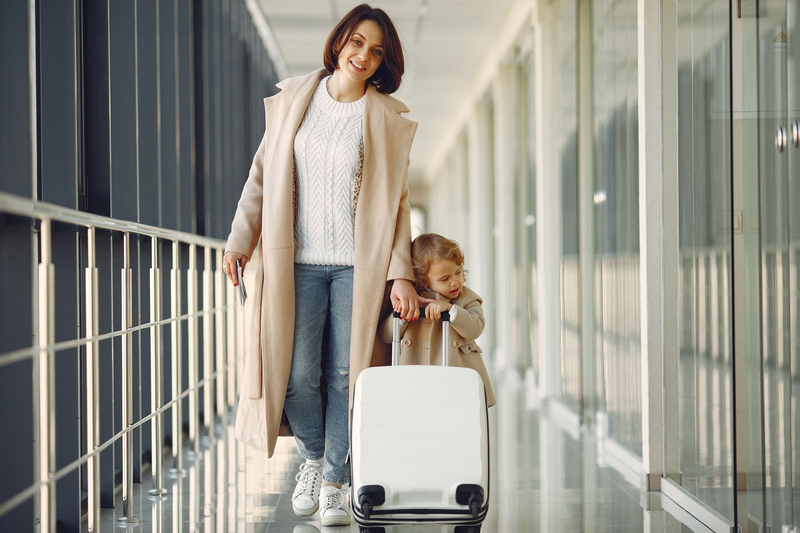 Mamă și fiică cu valiză în aeroport, în drum spre o nouă călătorie