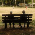 Doi vârstnici pe o bancă într-un parc, văzuți din spate