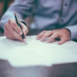 Mână care semnează un document cu pixul, imagine pentru o cerere small claims în UK