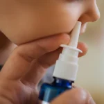 Părinte care ține un spray nazal lângă nasul unei fetițe